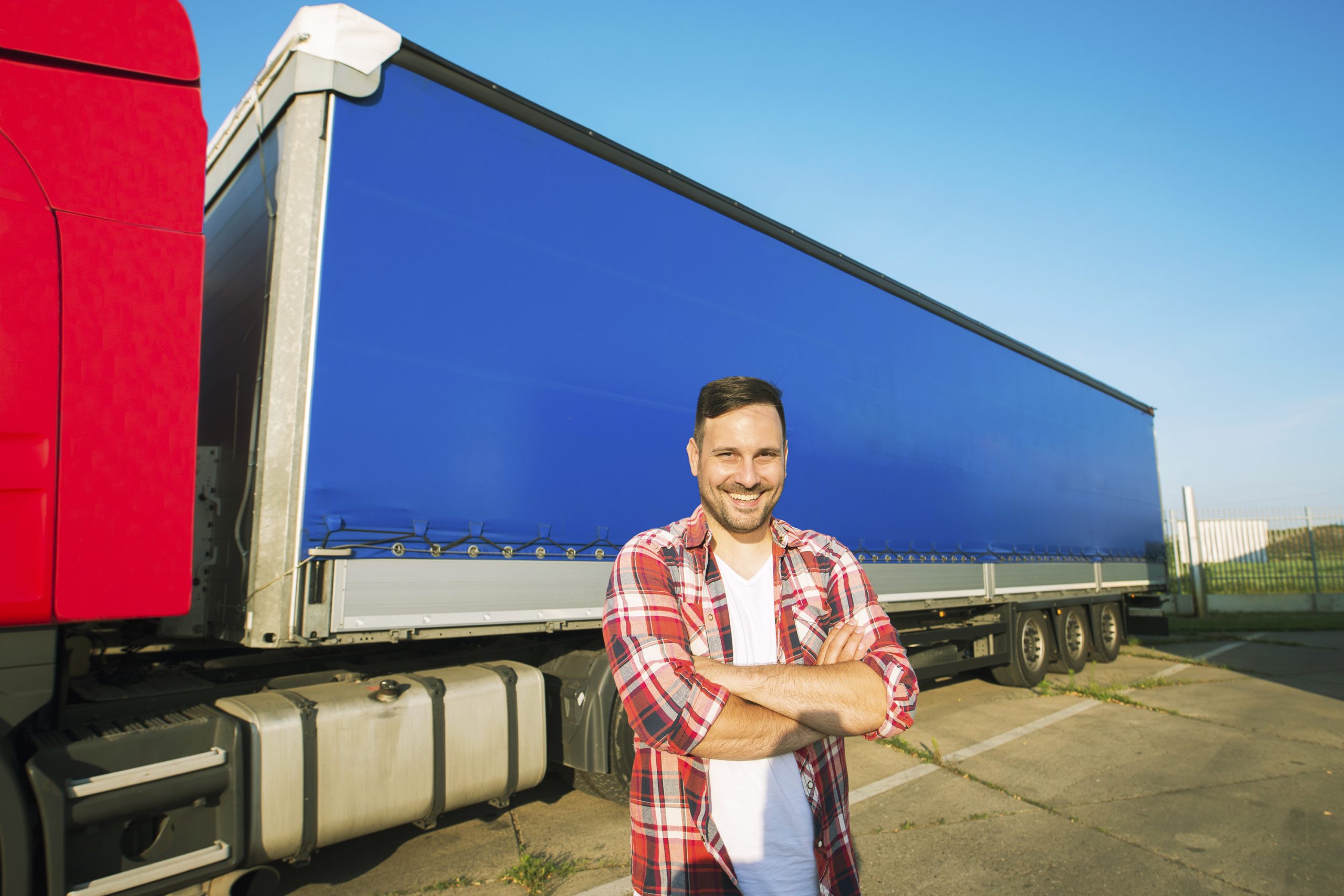 Portrait of middle aged caucasian trucker with arms crossed standing by truck trailer ready for driving.